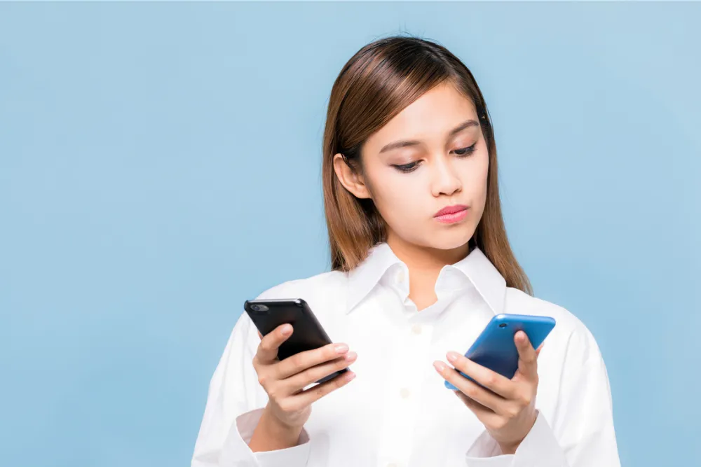 2つのスマホを見比べる女性