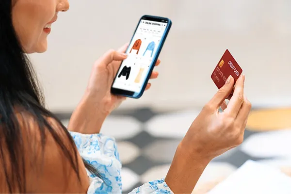 スマホとクレジットカードを持って、オンラインショッピングする女性