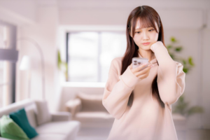 部屋でスマホを見て悩む女性