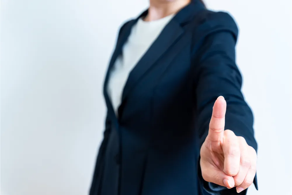人差し指を立てるスーツの女性